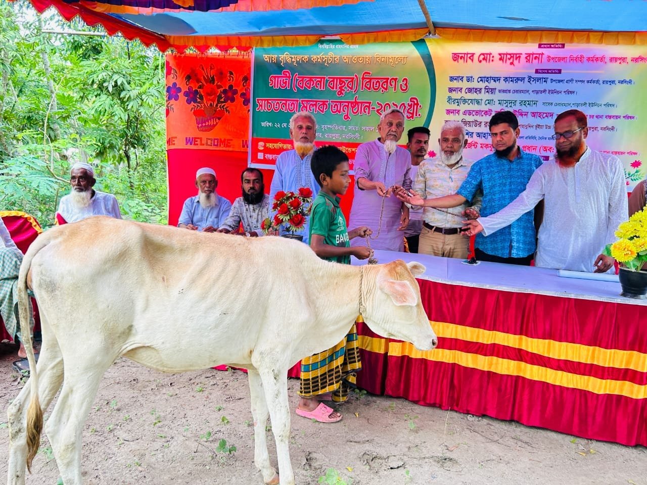 Cow distribution ceremony on a decorated stage, officials handing a cow to a family